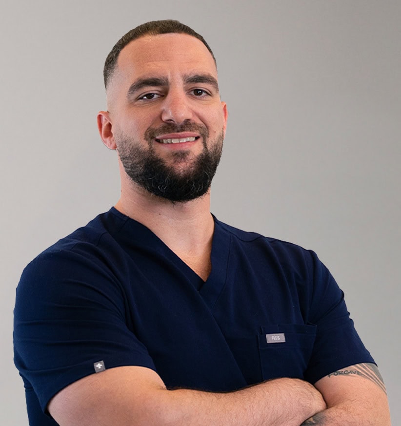Confident research management professional smiling with arms crossed, wearing navy scrubs.